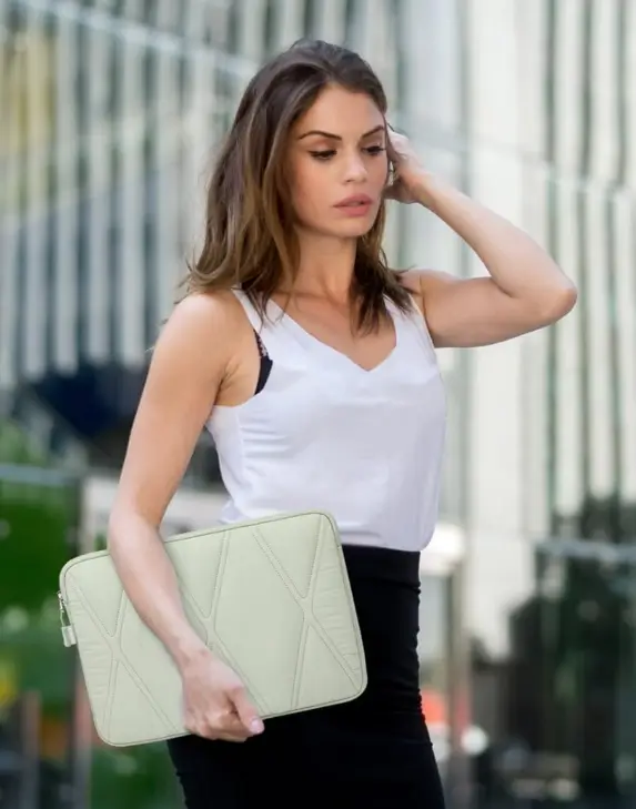 A woman walking outdoors carrying a mint green padded laptop sleeve under her arm